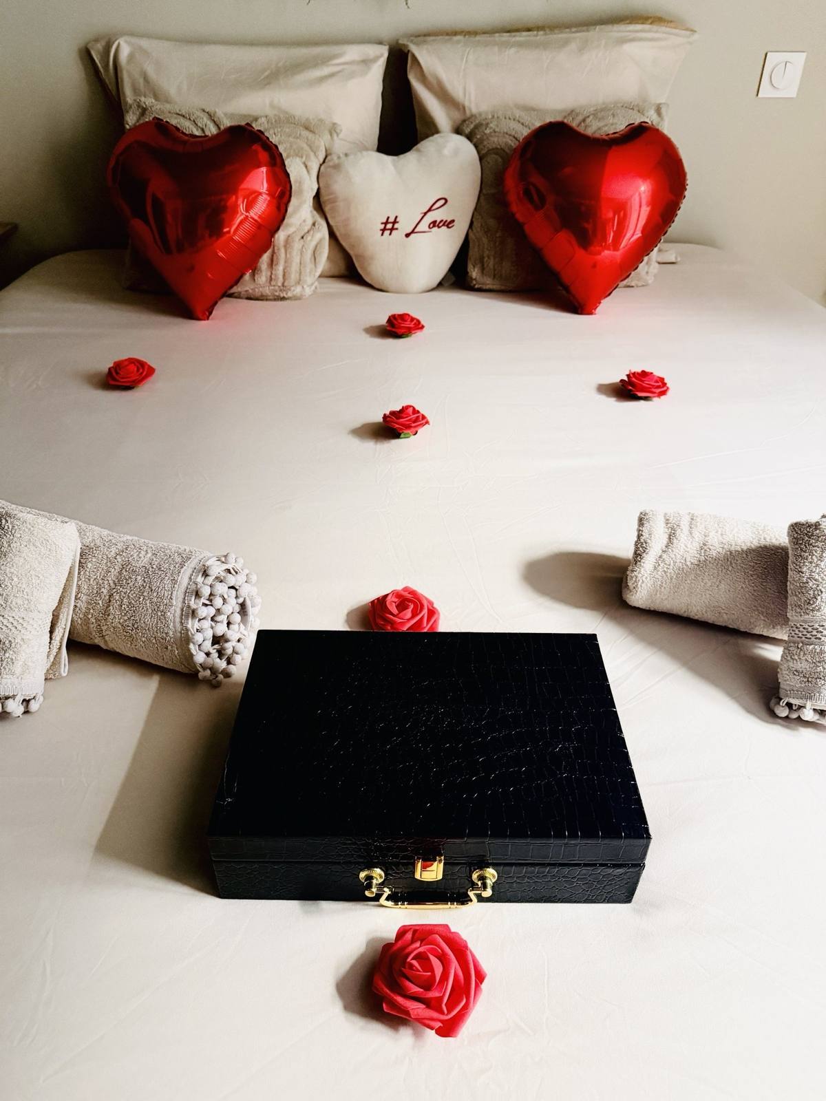 Coffret noir des extras posé sur le lit, entouré de roses