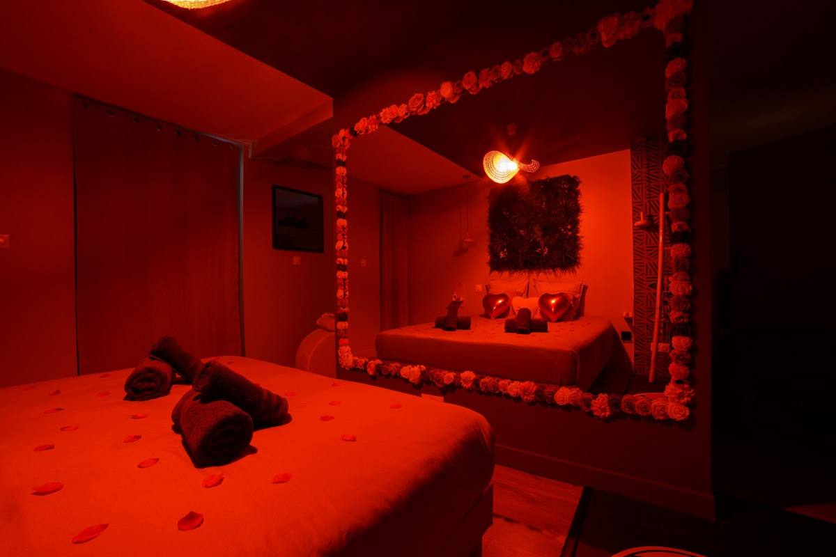 Lit King size face au grand miroir sous une lumière rouge tamisée, love room Amour & Bulles